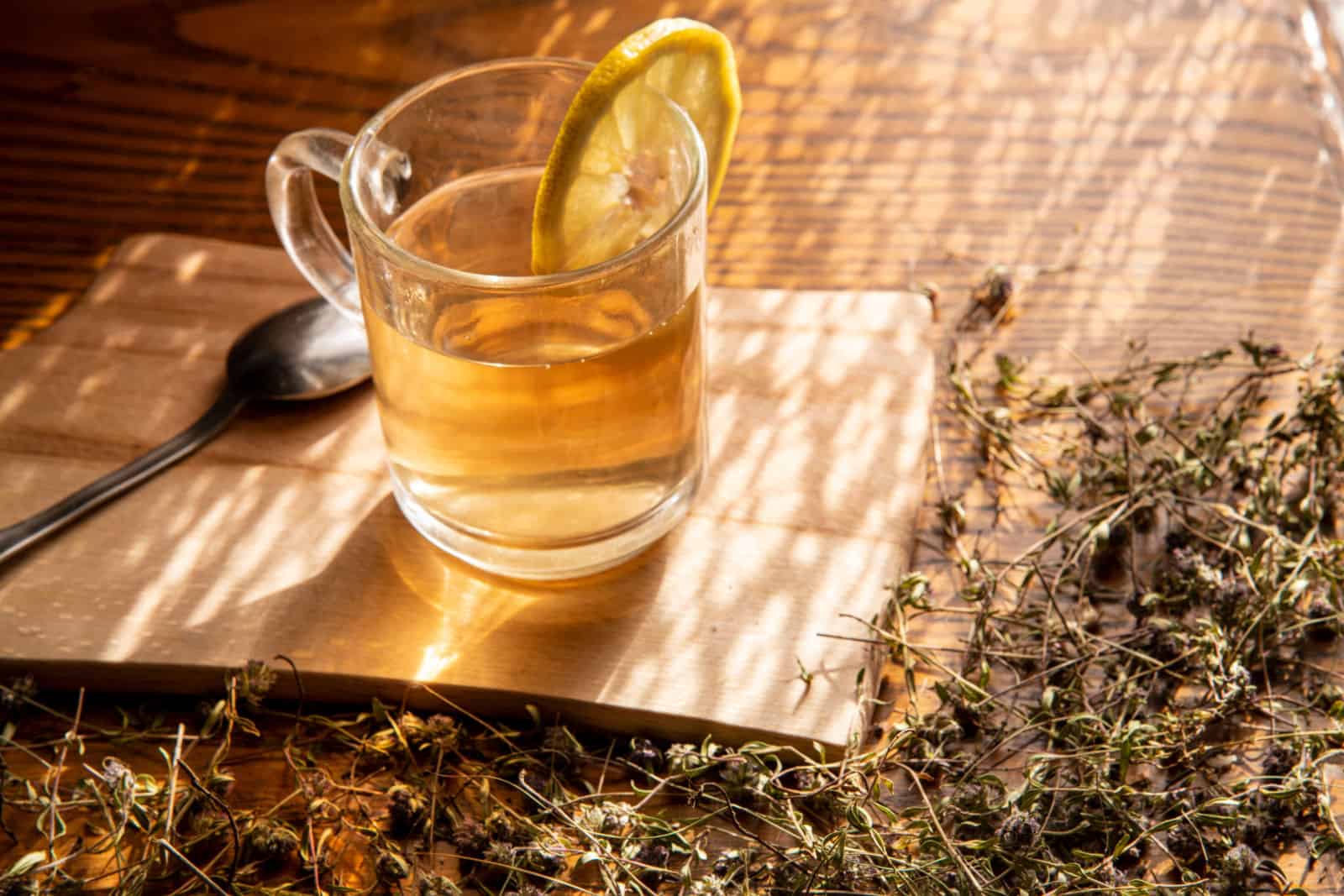 Una taza de té de tomillo rastrero (thymus serpyllum), con ramitas secas de tomillo rastrero sobre un fondo de madera